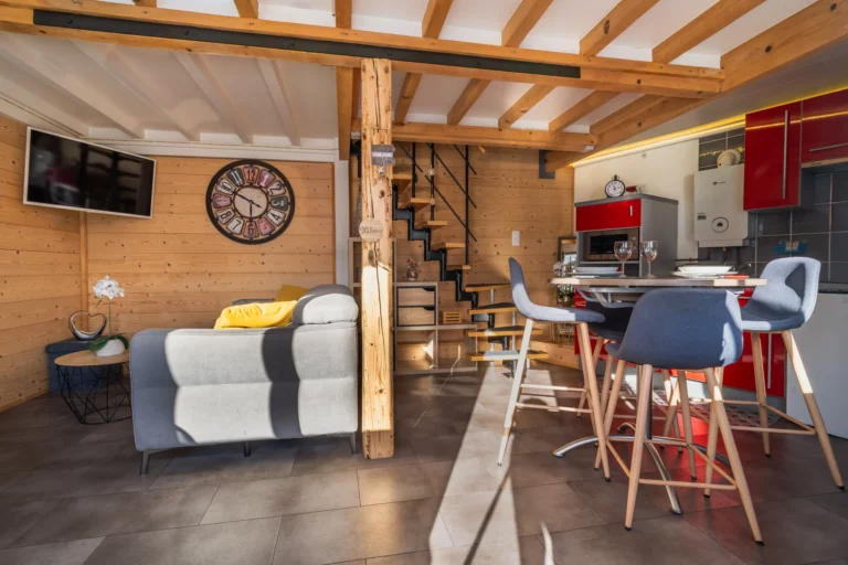 Pièce de vie du chalet avec cuisine, salon et escalier en bois – photo LLP Agency